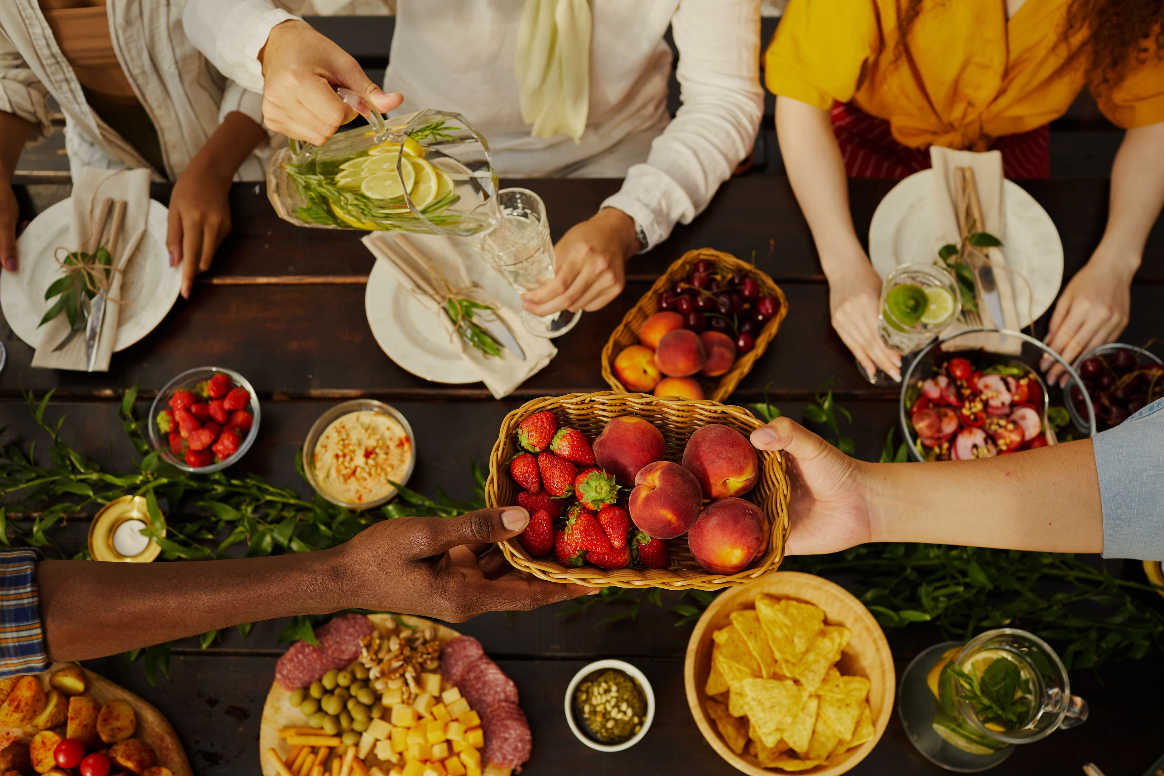 Hands passing a basket of strawberries and peaches across a dark wooden table.