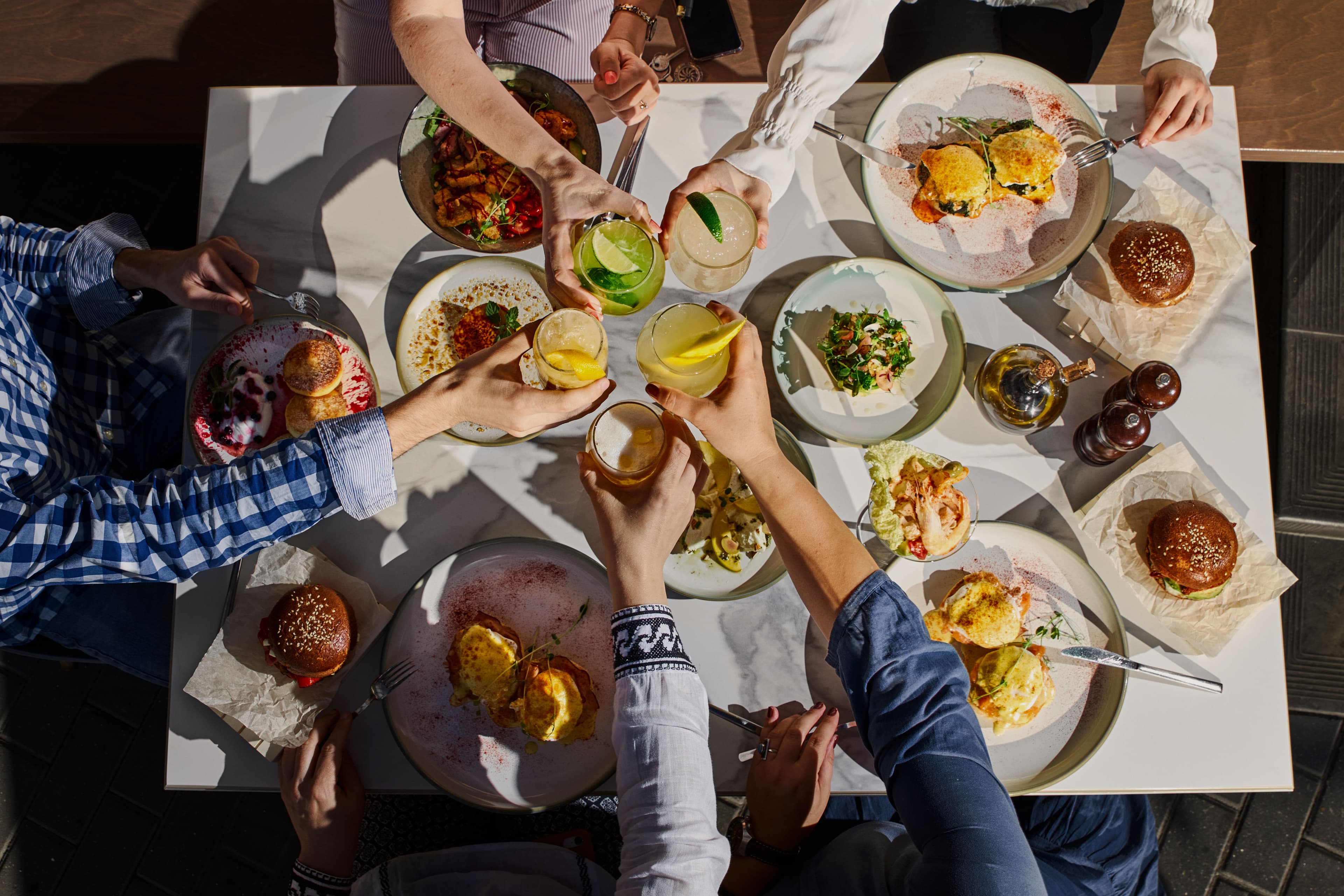 Overhead view of a table with several people's hands raising glasses together.